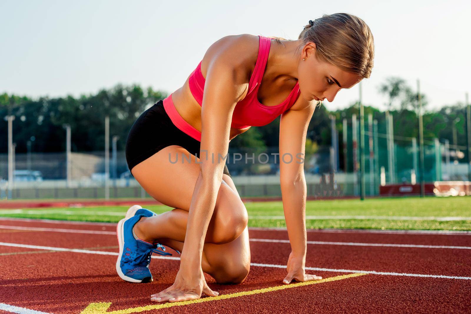 Young woman athlete at starting position ready to start a race. Female sprinter ready for sports exercise on racetrack.