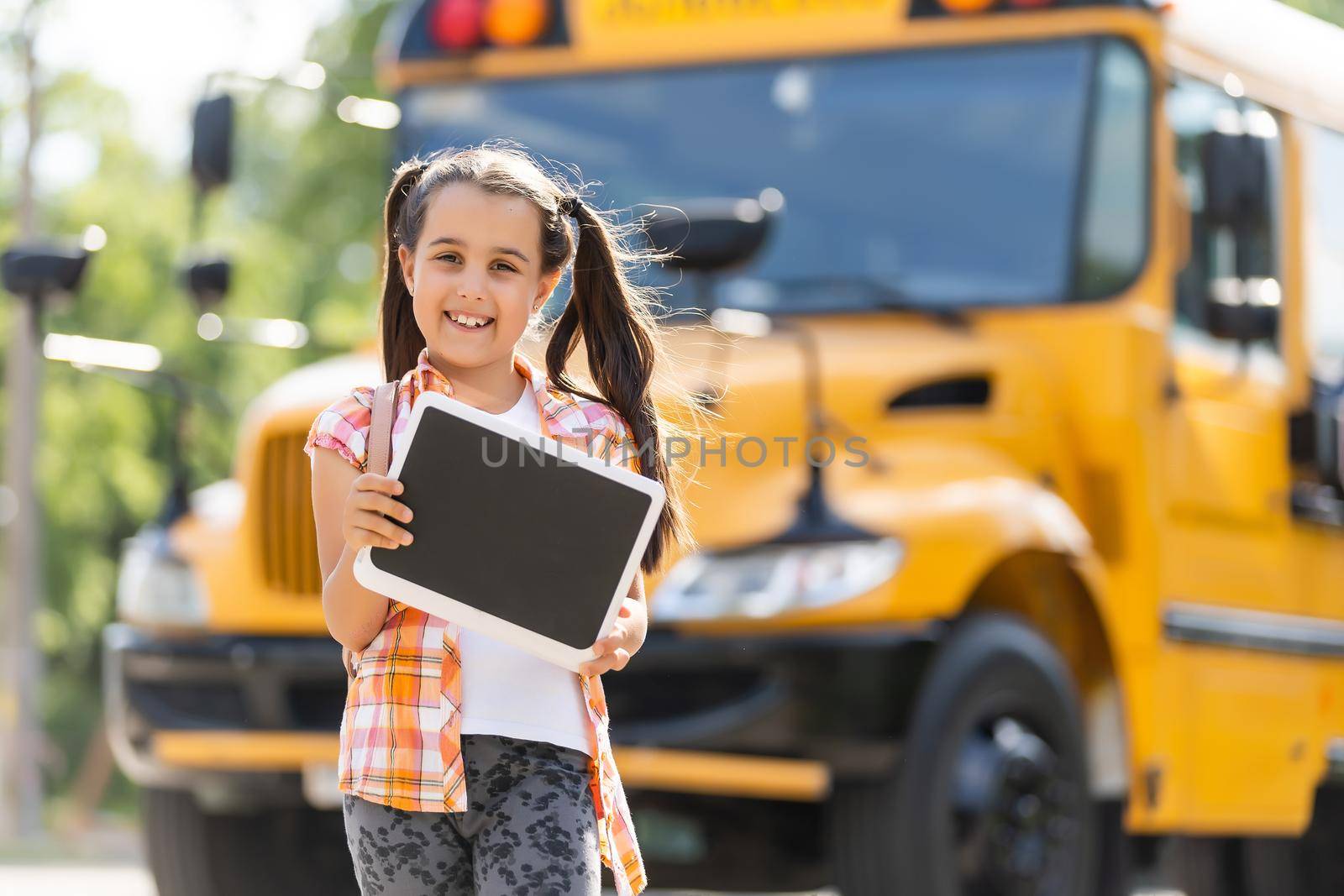 Little girl standing by a big school bus door with her backpack.