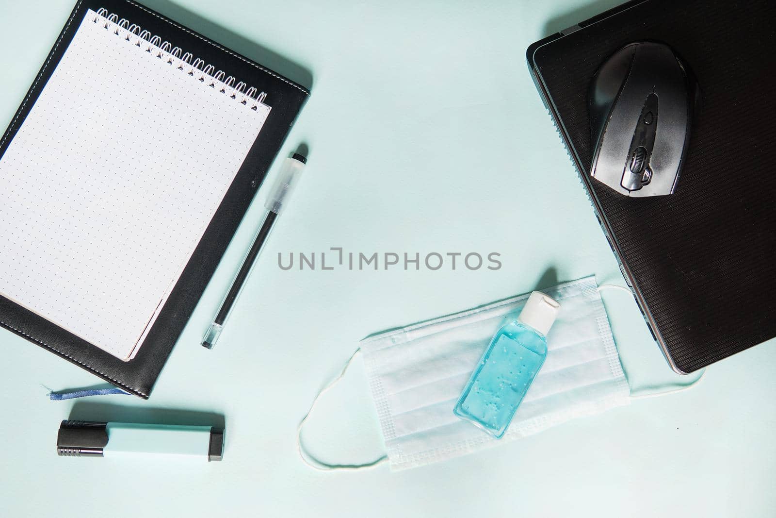 Top view of a desktop with notebooks, pens, and a laptop. Work from home using an online device, protection from coronavirus during the quarantine period. Protective masks and antiseptic on a mint background.