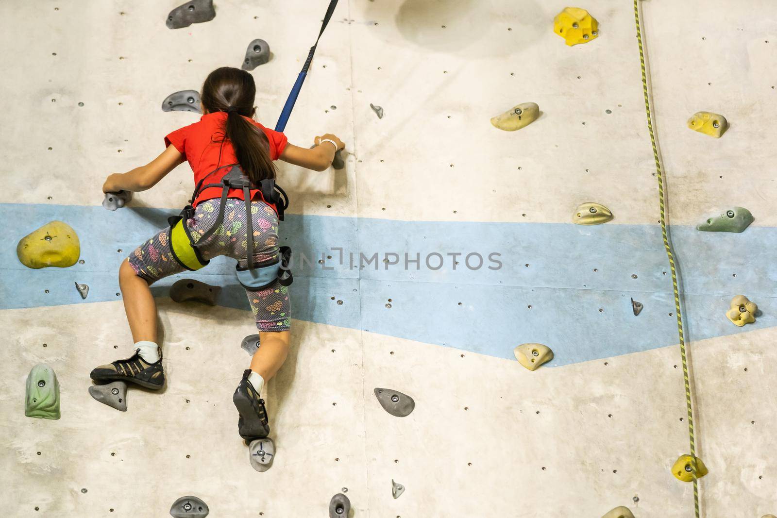 Sporty little girl climbing artificial boulder on practical wall in gym by Andelov13