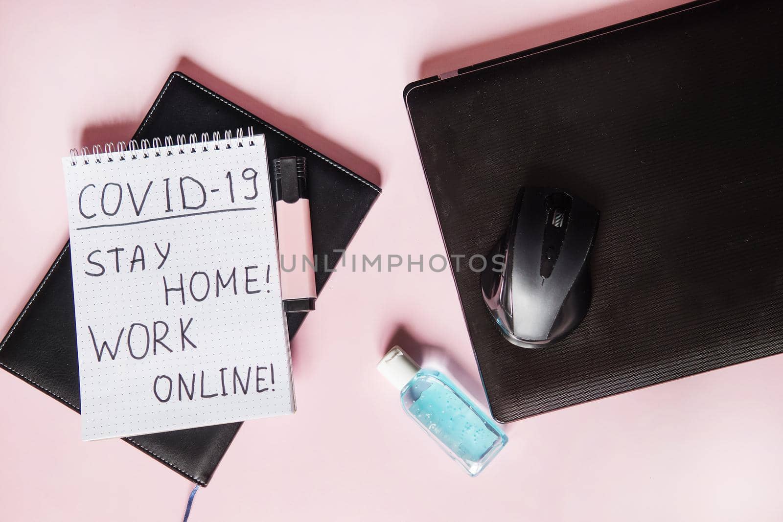 Top view of a desktop with laptops, a marker, and a laptop. Text Covid-19, stay at home, WORK ONLINE. Work from home using an online device, protection from coronavirus during the quarantine period. Pink background. Flat lay.