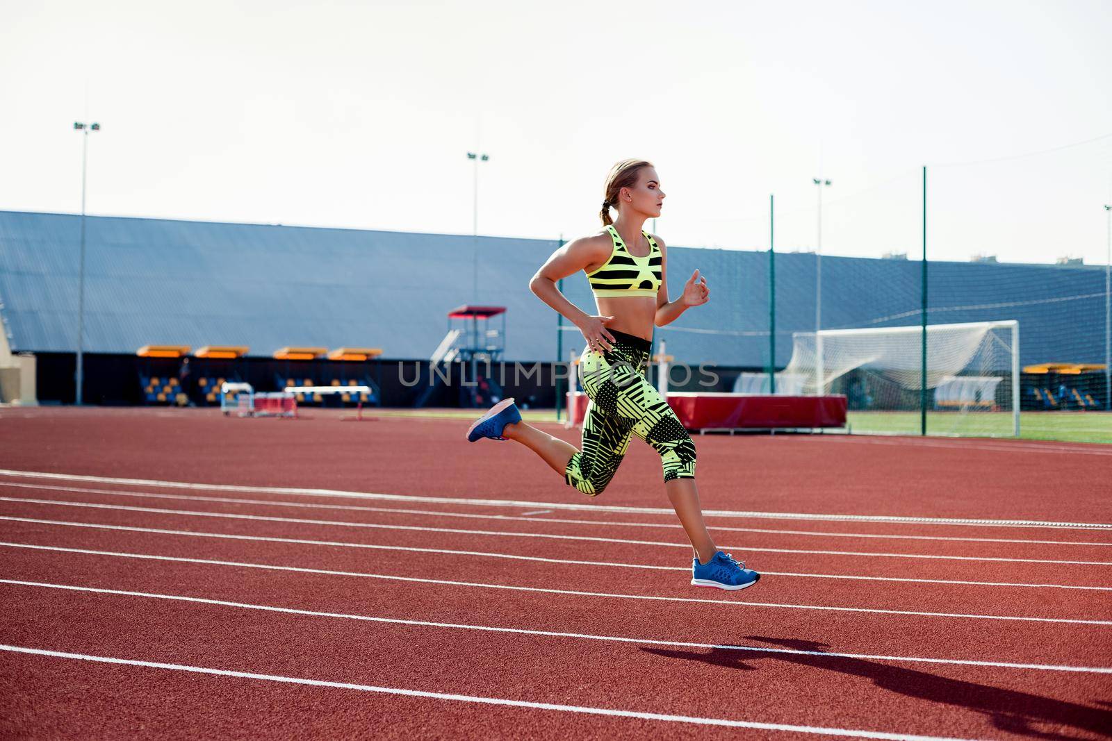 Beautiful young woman exercise jogging and running on athletic track on stadium. Red treadmill in sport field.