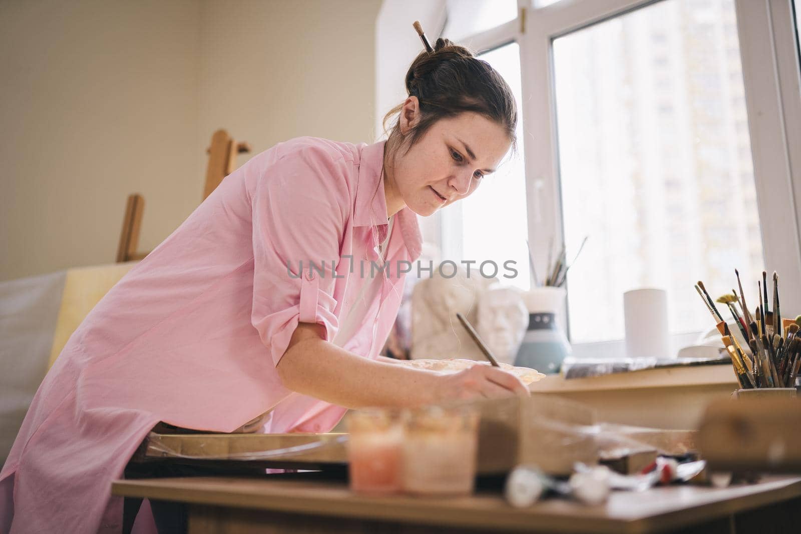 Female artist working in studio. Creative workspace, painting class, easel with canvas, art therapy. Inspiration, creativity, talent, craft concept. Artist studio interior. People, leisure and hobby by Tomashevska