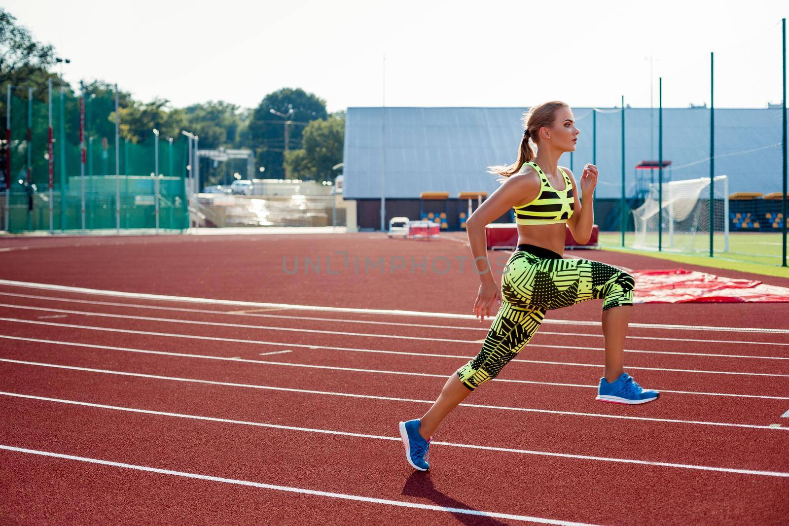 Beautiful young woman exercise jogging and running on athletic track on stadium. Red treadmill in sport field.