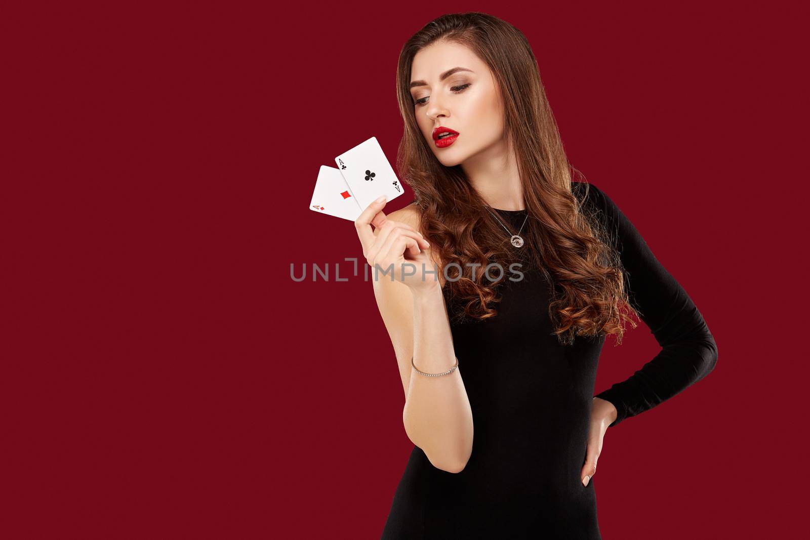 Beautiful caucasian woman in black dress with poker cards gambling in casino. Studio shot on red background. Poker. Two Aces in Hand
