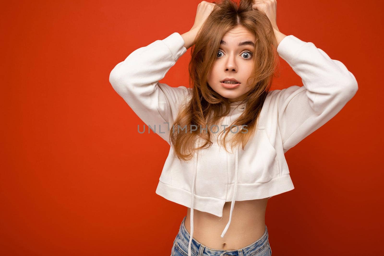 Young shocked amazed beautiful dark blond woman with sincere emotions isolated on background wall with copy space wearing casual white hoodie. Surprise concept.
