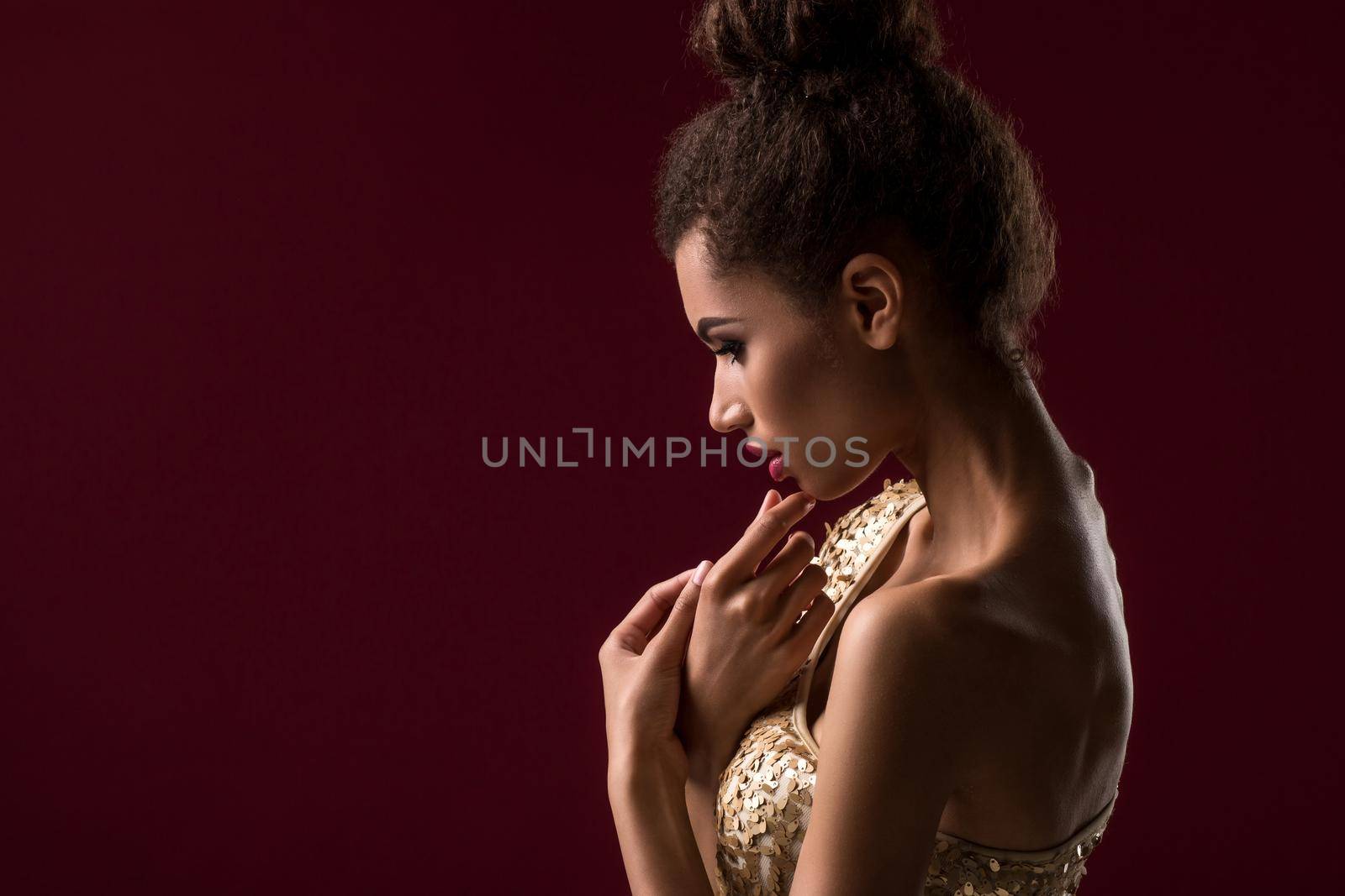 Fashion young African woman with makeup, in sexy gold dress. Model on a red background in the studio. A woman is half a turn