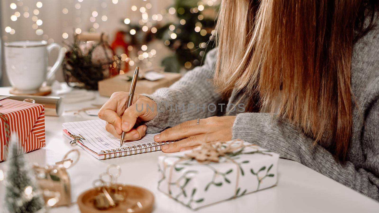 Goals plans make to do and wish list for new year christmas concept, girl writing in notebook. Woman hand holding pen on notepad at home on winter holidays xmas. Christmas decoration, gift boxes.
