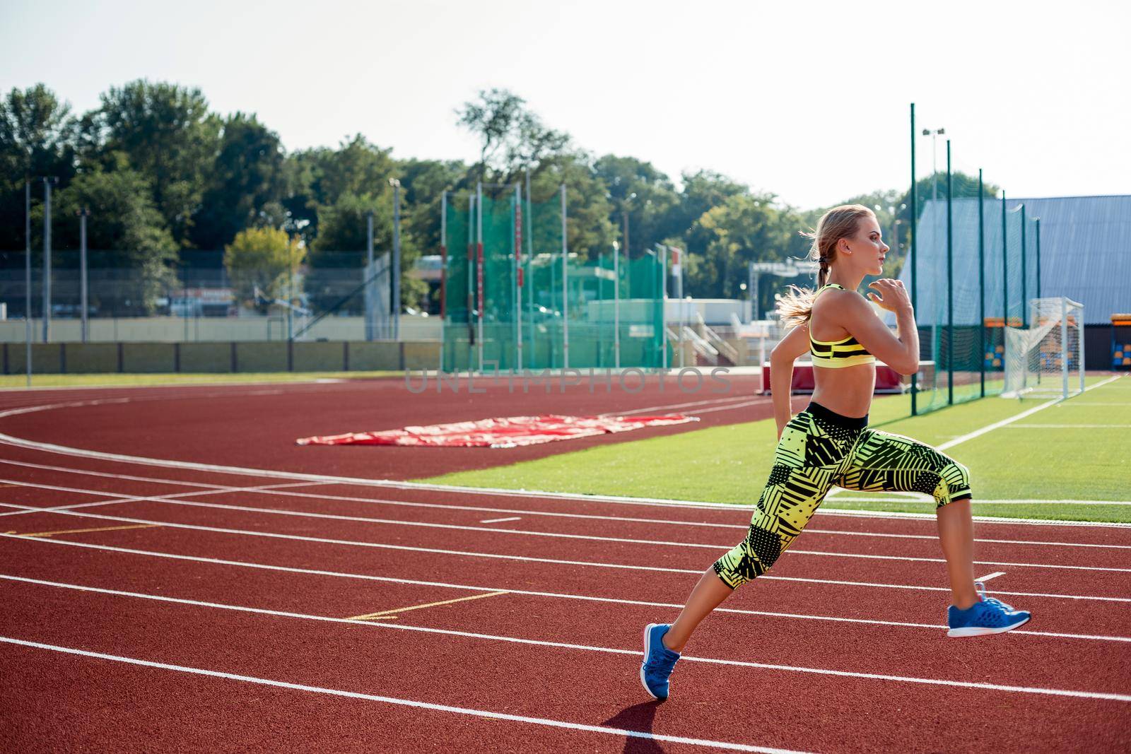Beautiful young woman exercise jogging and running on athletic track on stadium. Red treadmill in sport field.