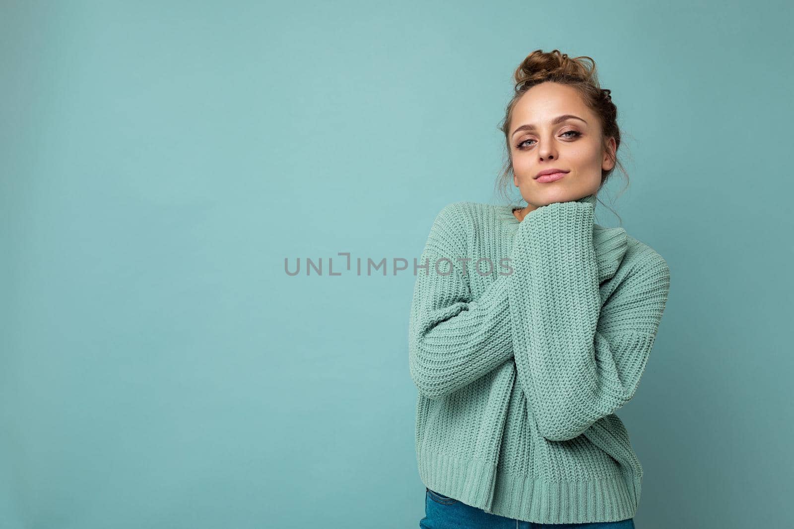 Portrait of young happy positive satisfied cute cozy attractive beautiful blonde woman with sincere emotions wearing casual blue pullover isolated on blue background with copy space by TRMK