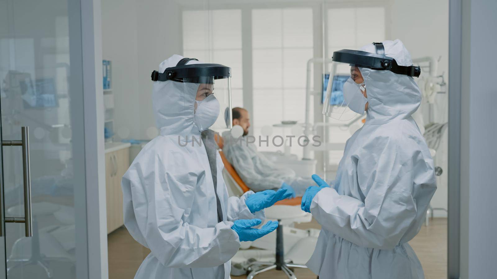 Dentists with virus protection suits talking about dental procedure by DCStudio