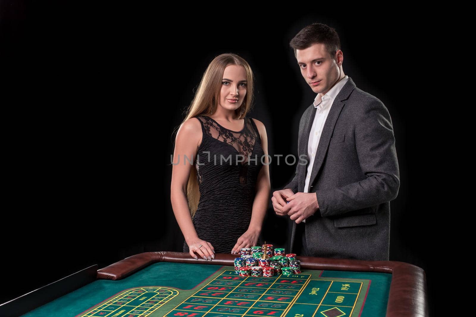 Elegant couple at the casino betting on the roulette, on a black background. A man in a suit with a beautiful young woman in a black dress