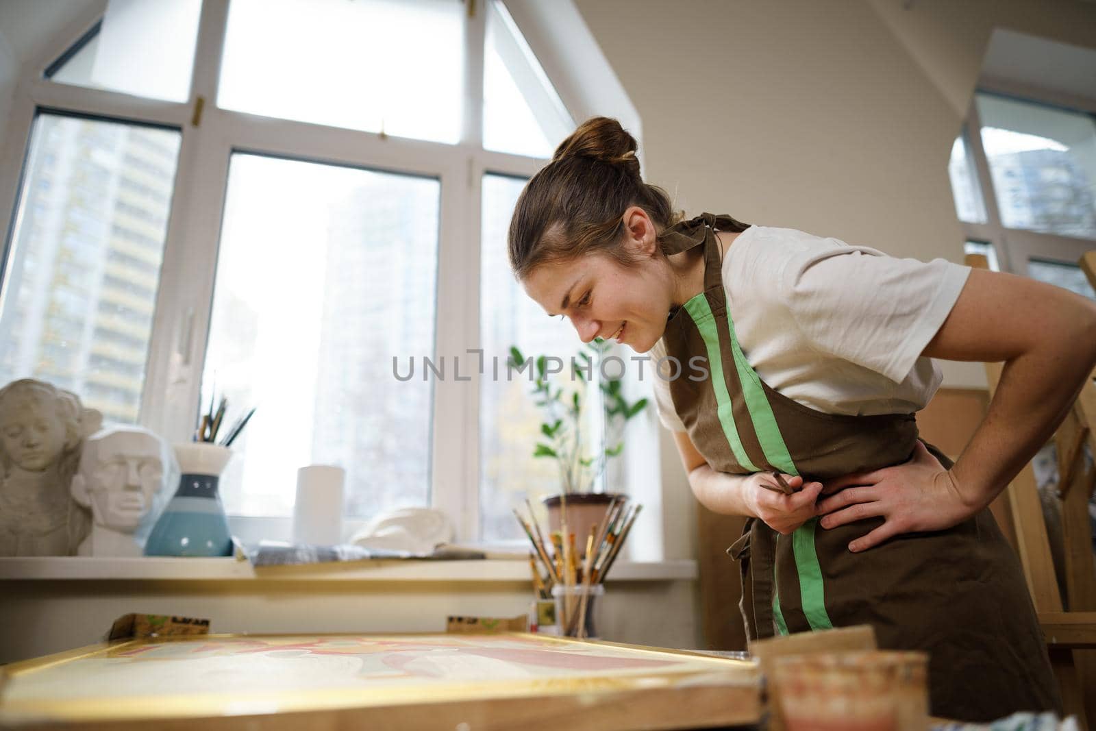 Cute woman paints on canvas in an art workshop. Artist creating picture. Art school or studio. Work with paints, brushes and easel. Hobby and leisure concept. Woman painter at workspace.