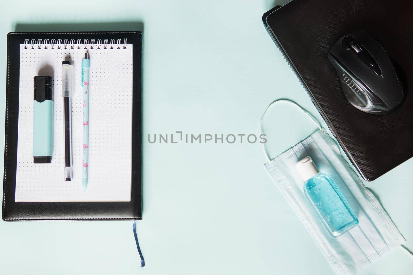 Top view of a desktop with notebooks, pens, and a laptop. Work from home using an online device, protection from coronavirus during the quarantine period. Protective masks and antiseptic on a mint background.