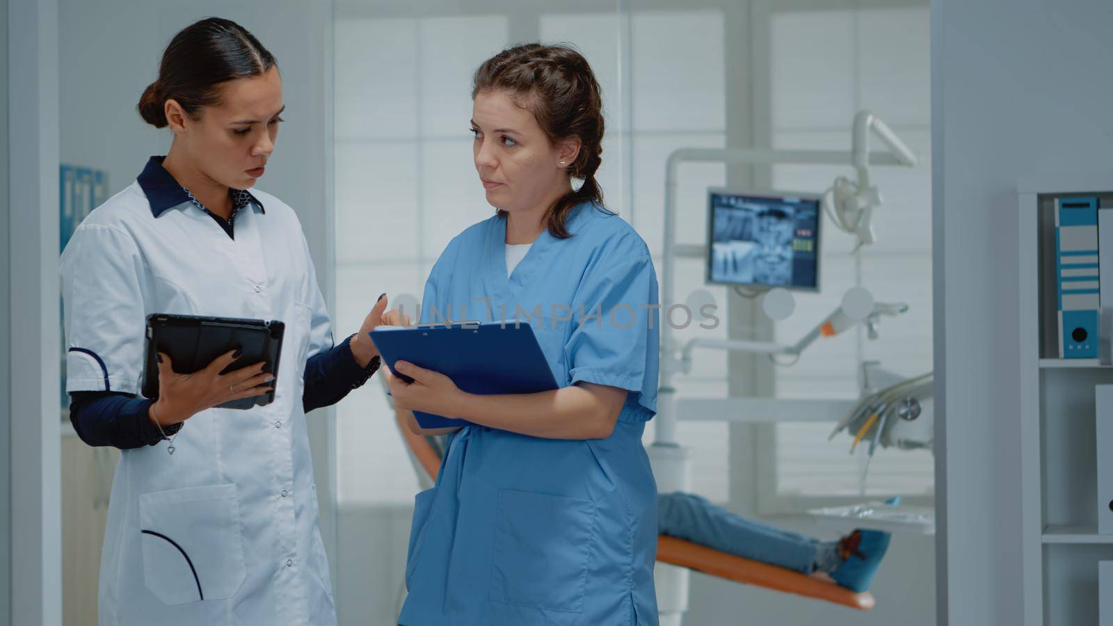 Orthodontists working team discussing dental operation at clinic. Dentist and assistant standing in stomatological cabinet while talking about oral equipment and teeth examination