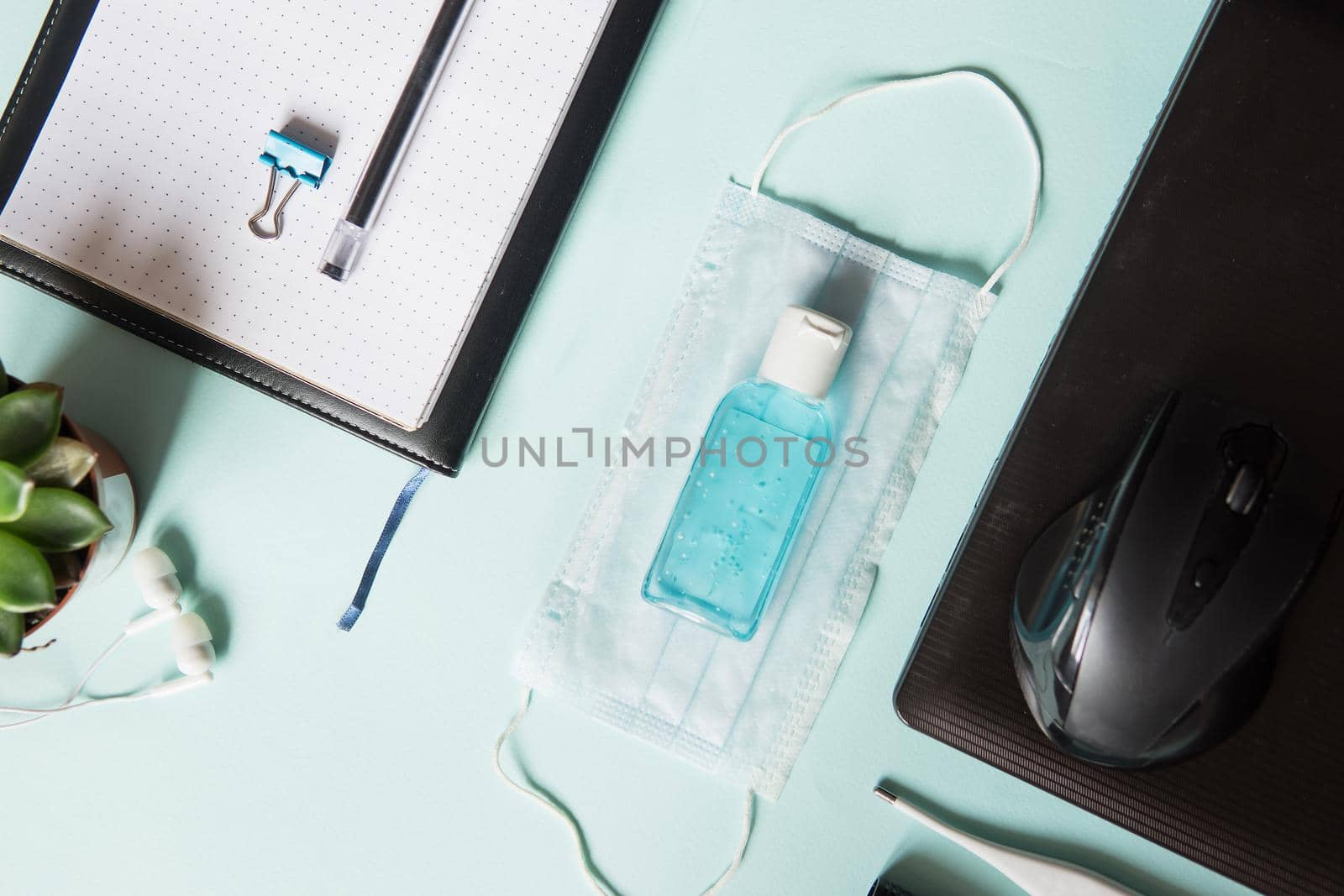Top view of a desktop with notebooks, pens, and a laptop. Work from home using an online device, protection from coronavirus during the quarantine period. Protective masks and antiseptic on a mint background.