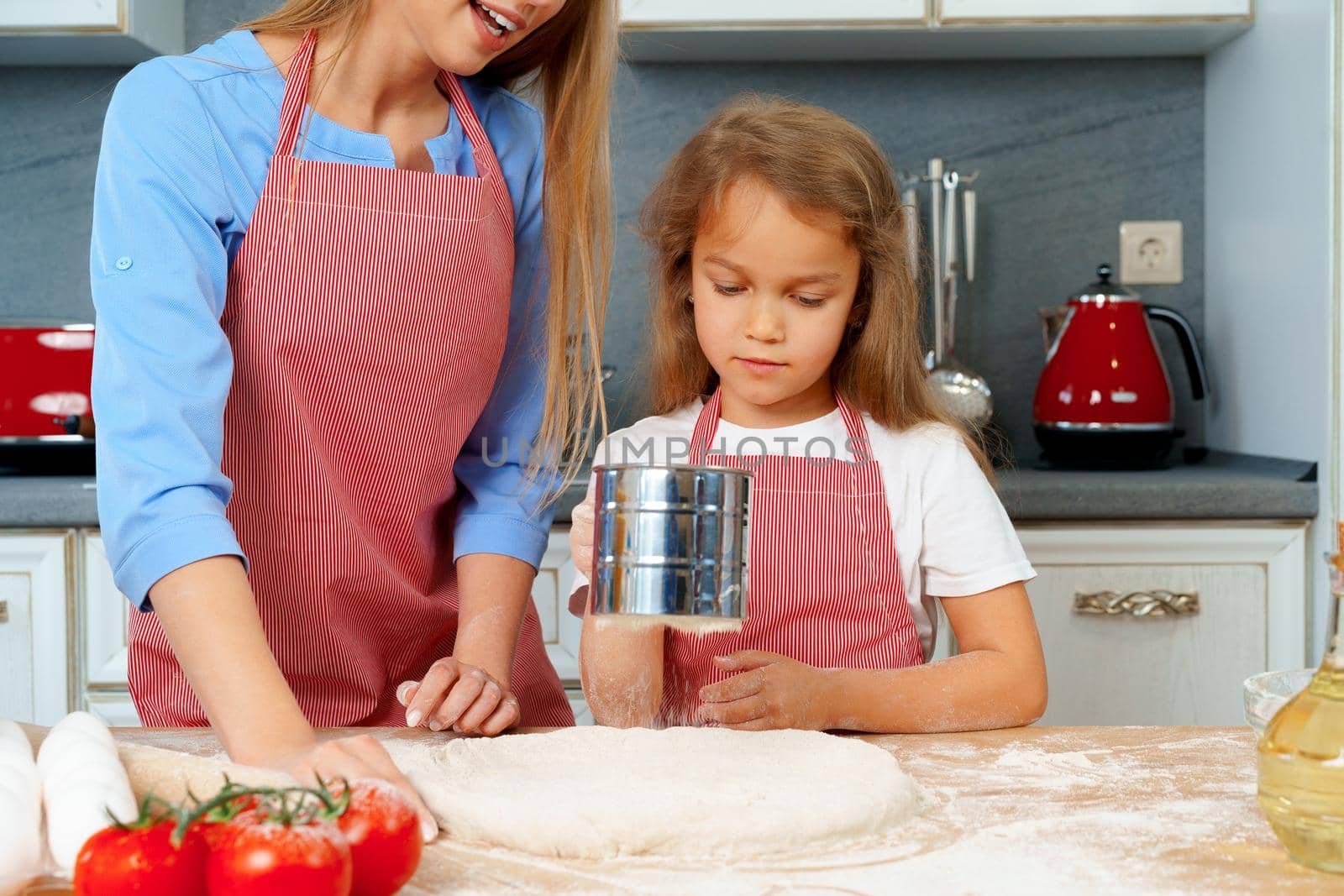 Mother and her little daughter preparing dough in kitchen close up