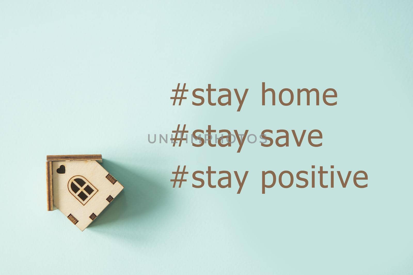 Text Stay home. Concept of self-quarantine at home as a preventive measure against an outbreak of the virus. Flat lay with an inspired quote, staying at home during the pandemic. Wooden house on a mint background.