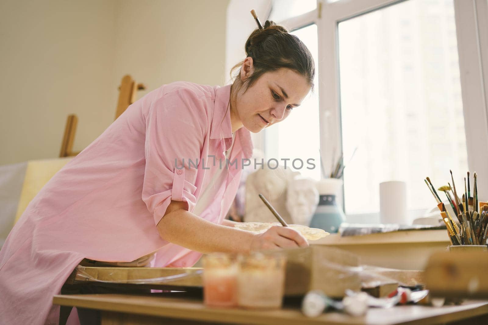 Art, creativity, hobby and creative occupation concept. Bringing creativity to life. Woman painting in art studio. Attractive female artist painting in workshop. Woman hobby, activity, profession by Tomashevska