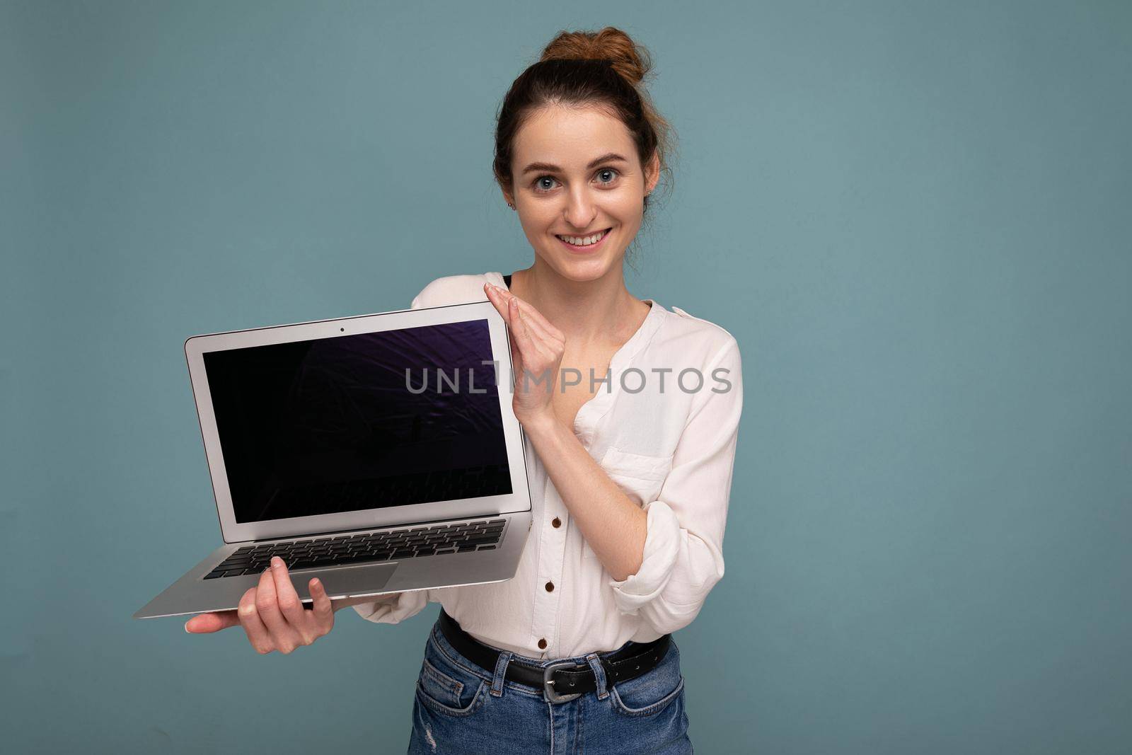 Beautiful smiling young woman holding netbook computer looking at camera wearing white shirt isolated on blue background. Copy space
