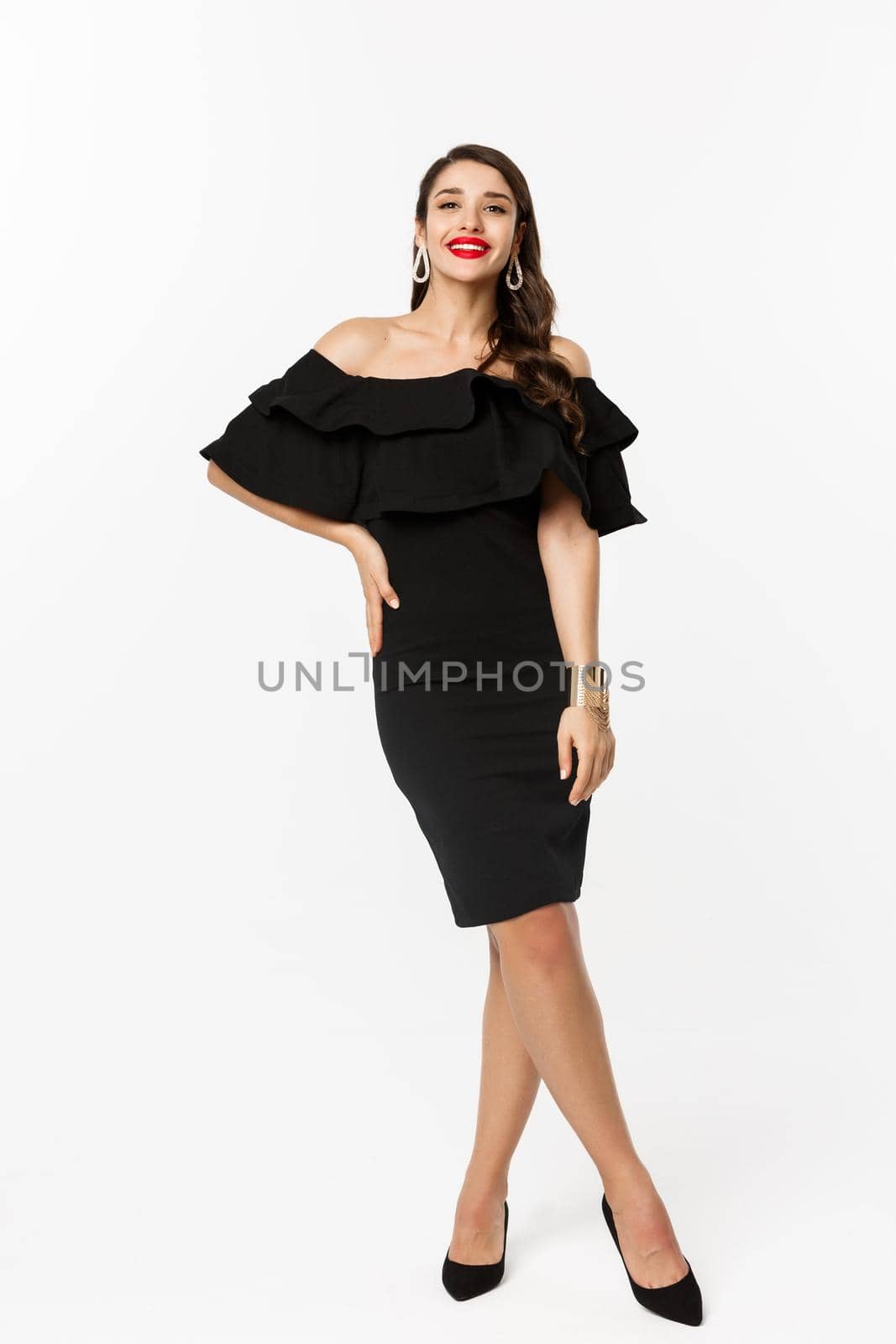 Beauty and fashion concept. Full length shot of beautiful brunette woman wearing luxury black dress and heels on party, smiling with red lips, standing over white background by Benzoix
