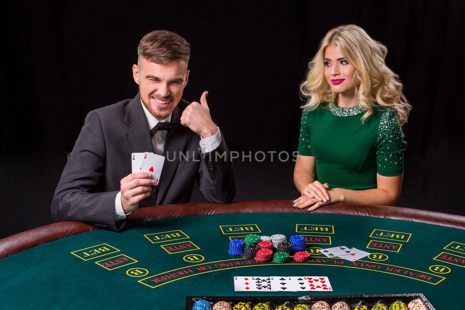 couple playing poker at the green table. The blonde girl and a guy in a suit. happy win, two aces