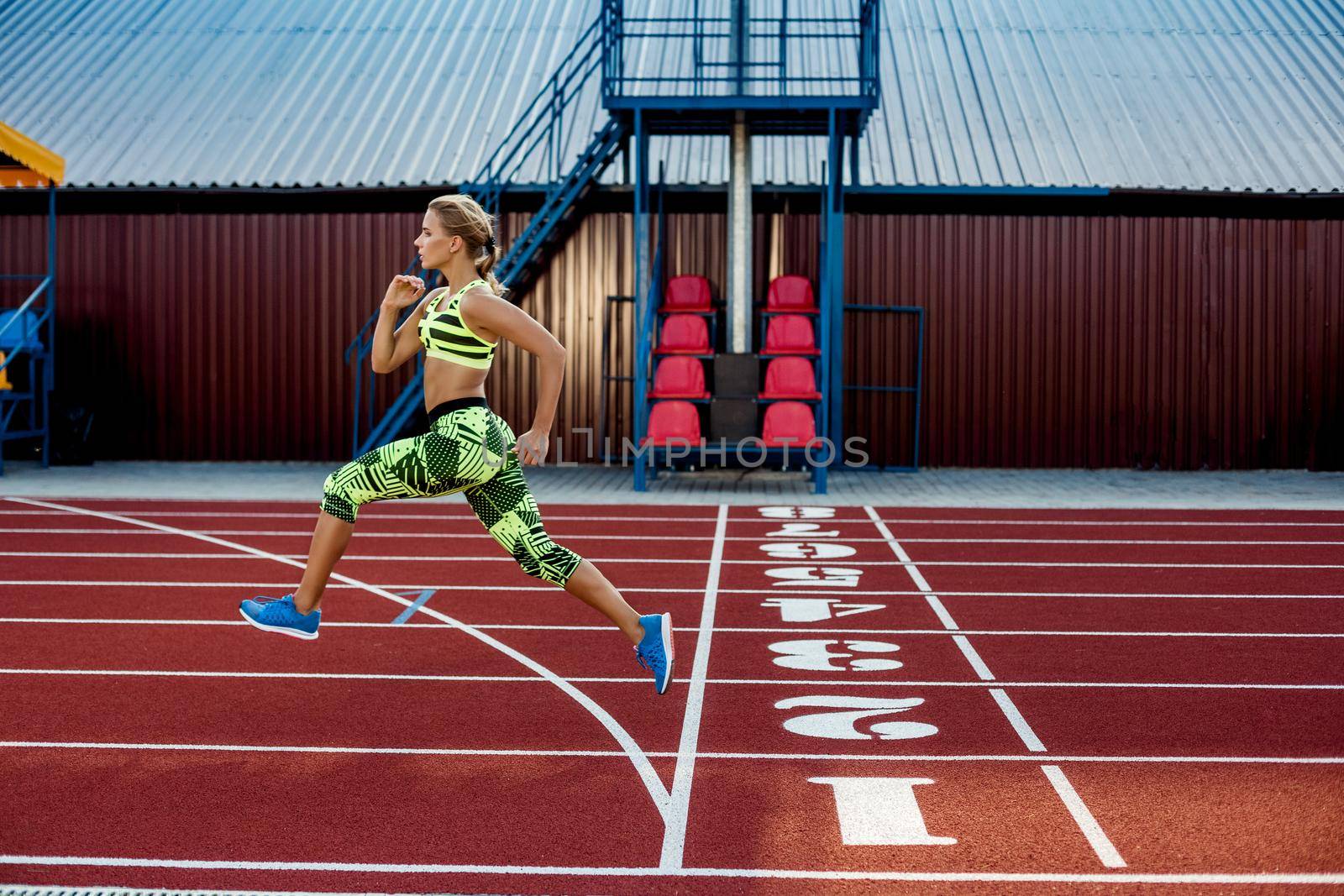 Young, beautiful girl athlete in sportswear runs along the treadmill. Sport background. Outdoor stadium