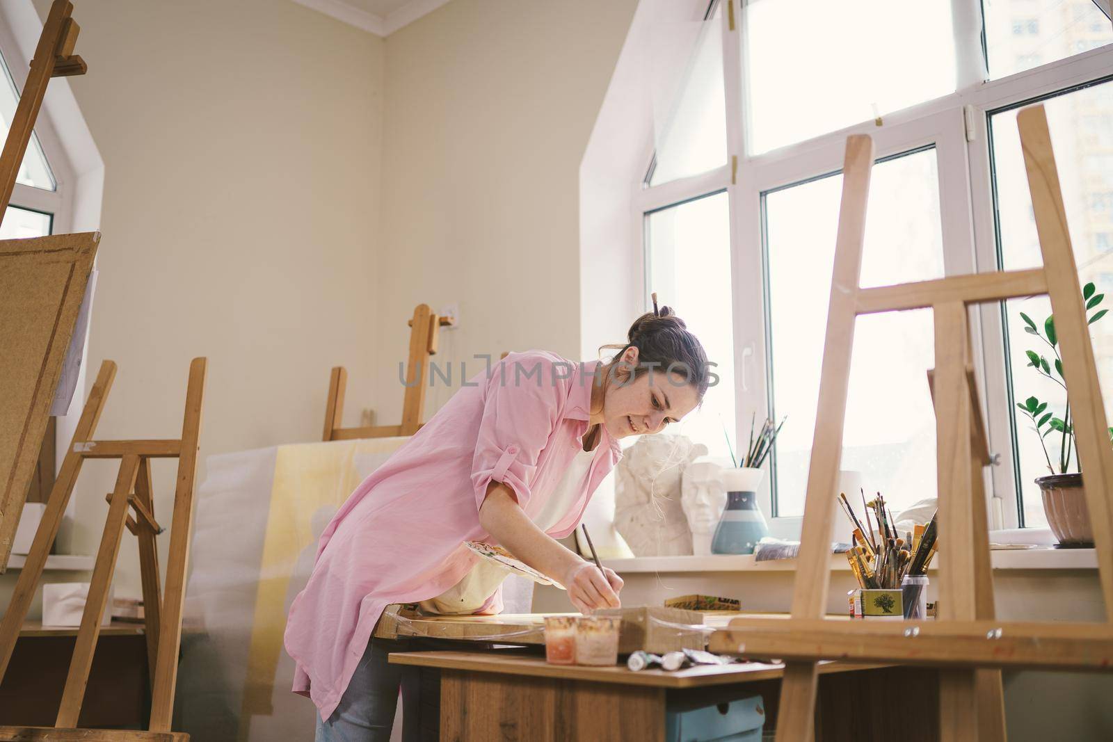 Female artist working in studio. Creative workspace, painting class, easel with canvas, art therapy. Inspiration, creativity, talent, craft concept. Artist studio interior. People, leisure and hobby by Tomashevska