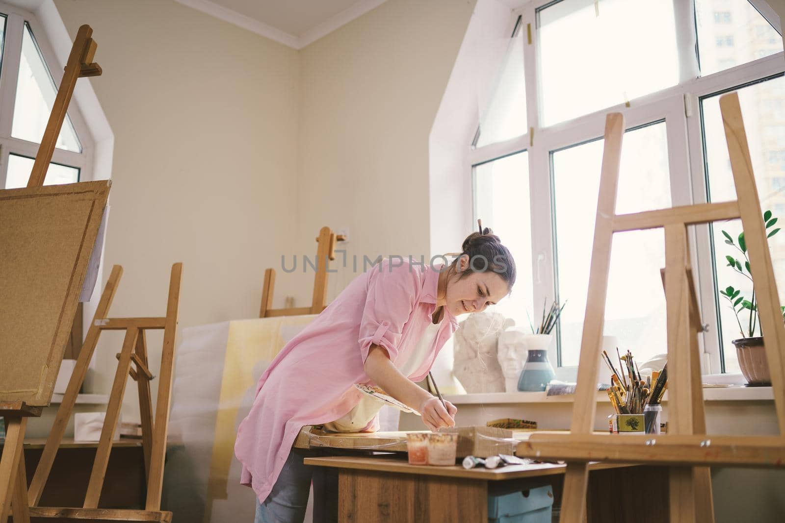 Art, creativity, hobby and creative occupation concept. Bringing creativity to life. Woman painting in art studio. Attractive female artist painting in workshop. Woman hobby, activity, profession by Tomashevska