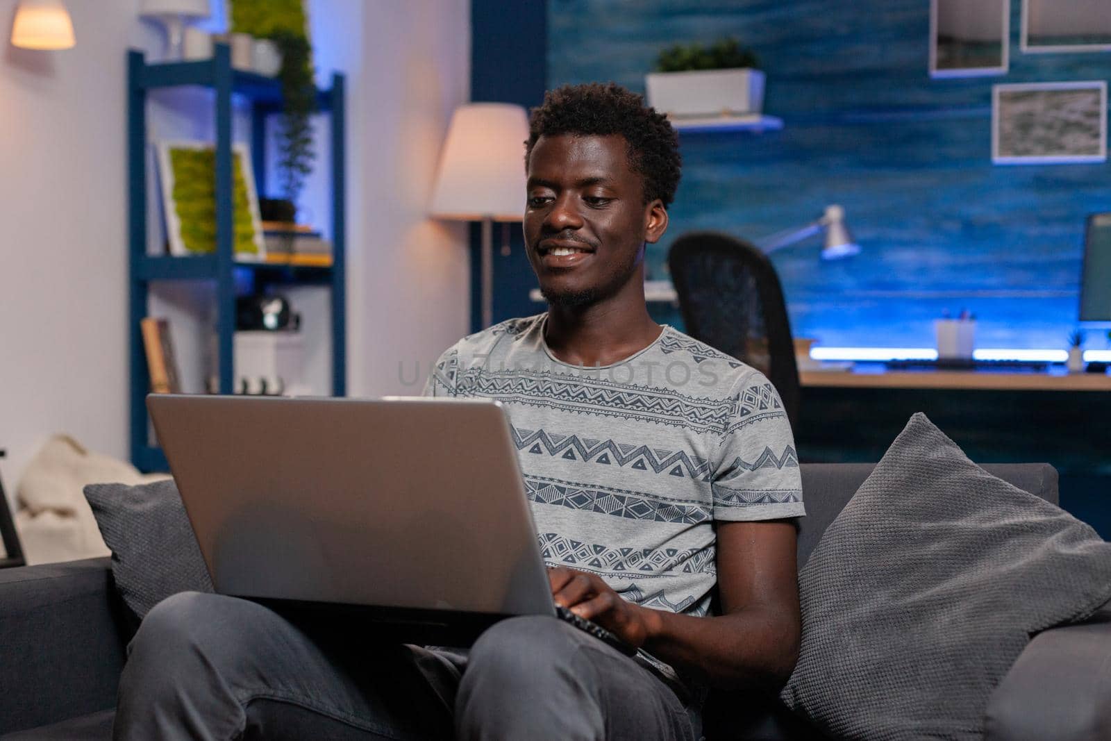 African american employee sitting on couch browsing communication information working remote from home at virtual project. Black young entrepreneur analyzing financial graph on laptop