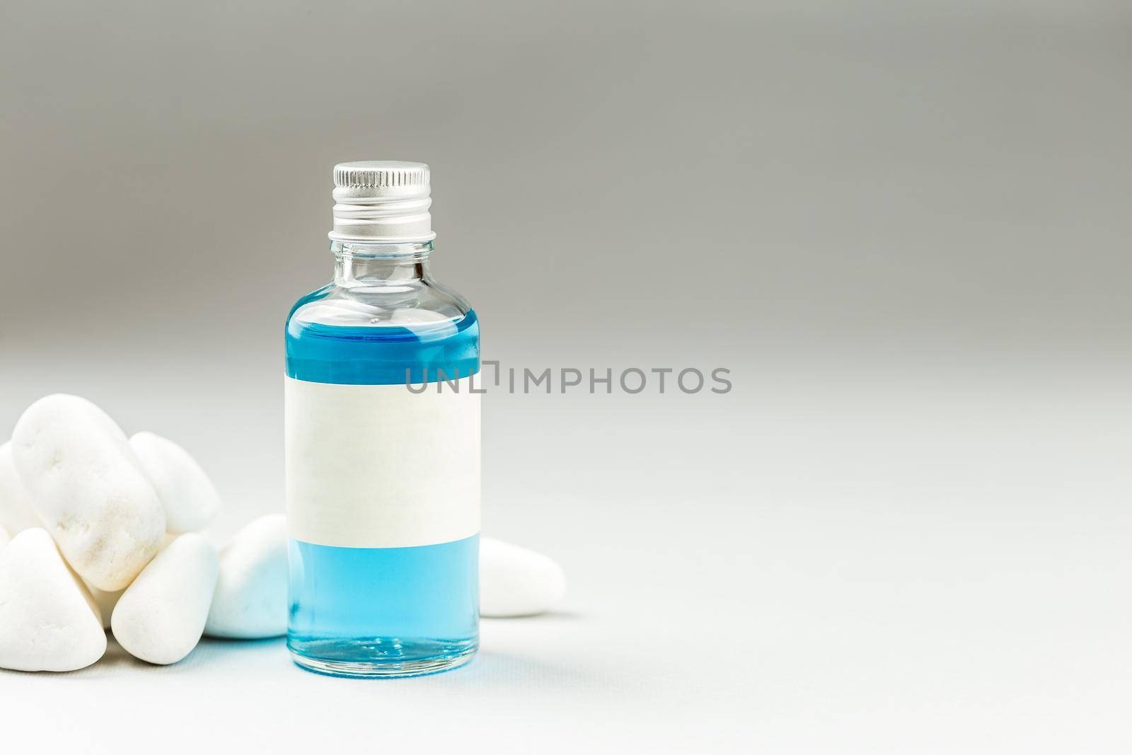 Plastic Free Cosmetic Packaging, Glass Bottle with Metal Cap and blank white Label on minimalistic gray background with white stones decoration
