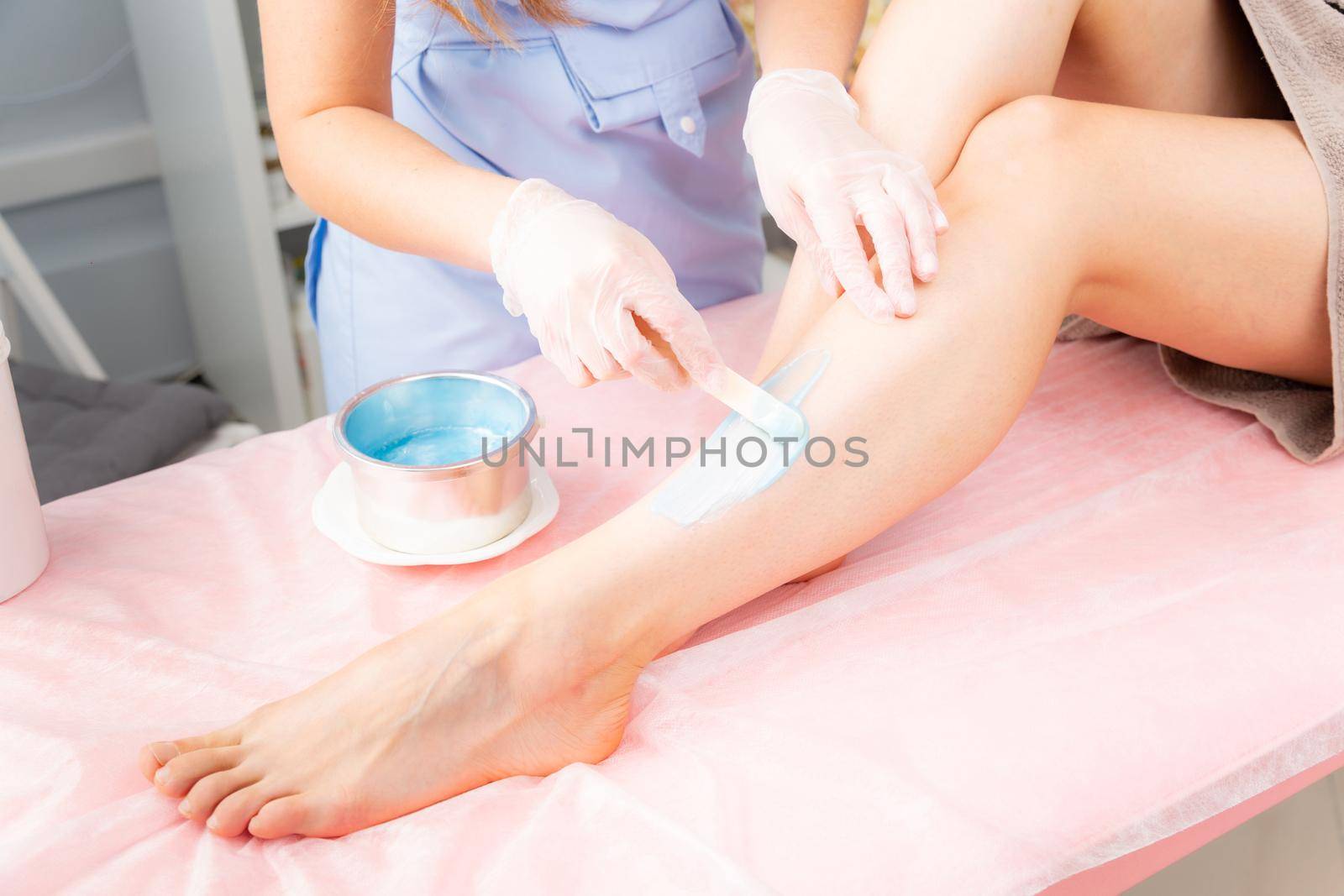 Sugar and waxing depilation of the feet in the beauty salon. Rid of hair on the legs. Sugaring. Master cosmetologist removing hair on the legs. Beautician in the spa center. Cosmetology concept. by bashta