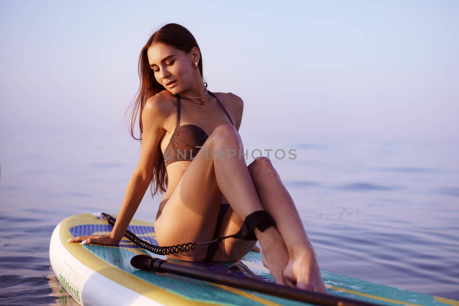 Young woman with sexy fit body posing on paddle board in the sea, close up