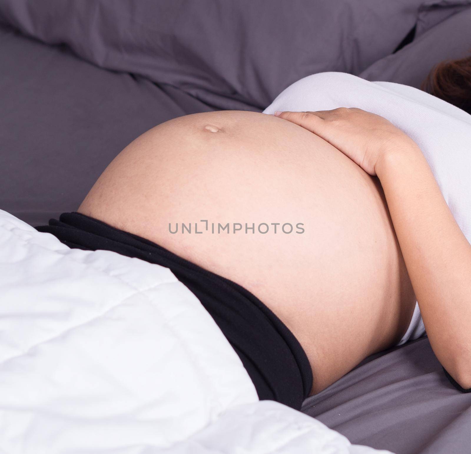 close up belly of pregnant woman sleeping on bed in the bedroom at home