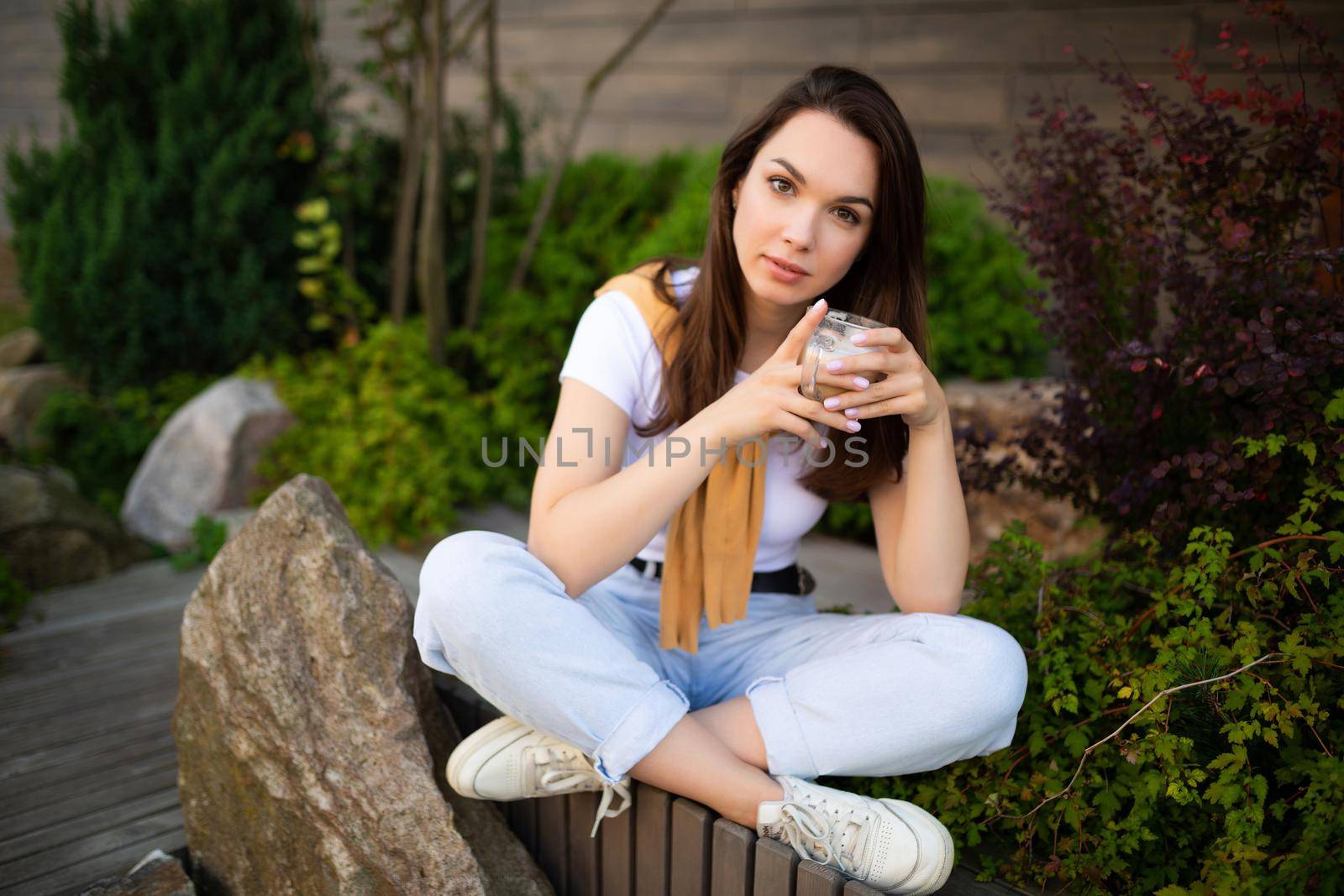 happy young woman sitting in a beautiful park and drinking spicy latte by TRMK