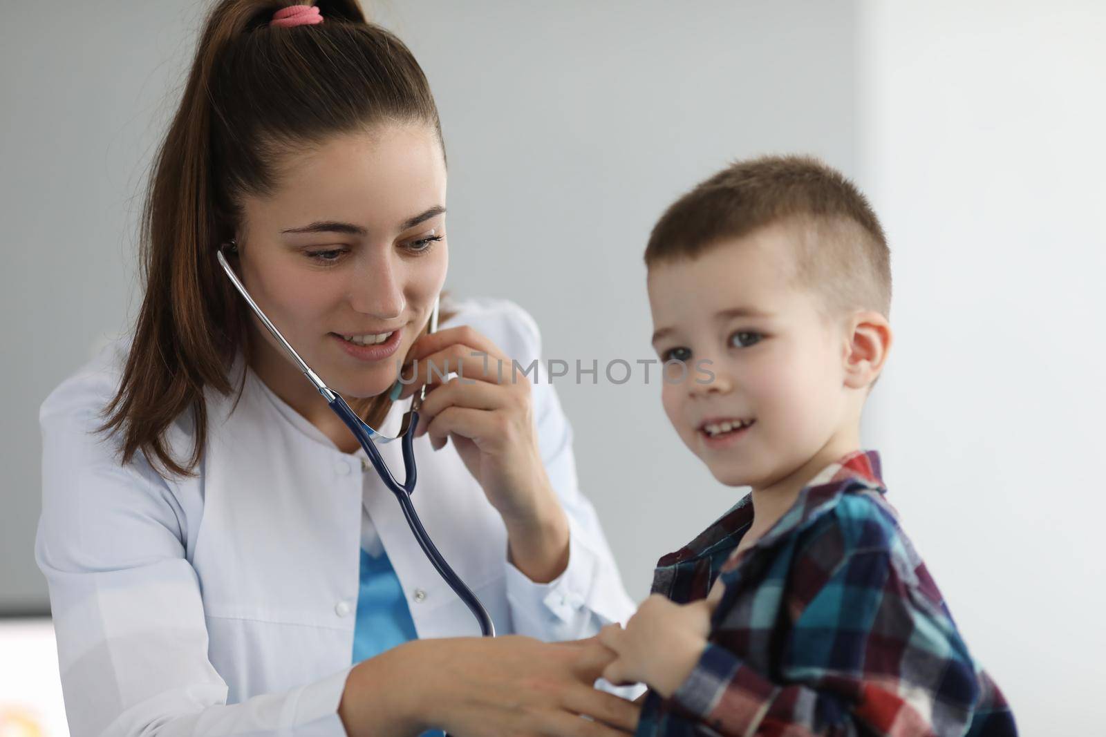 Doctor pediatrician listening to heart with stethoscope to little boy in clinic by kuprevich