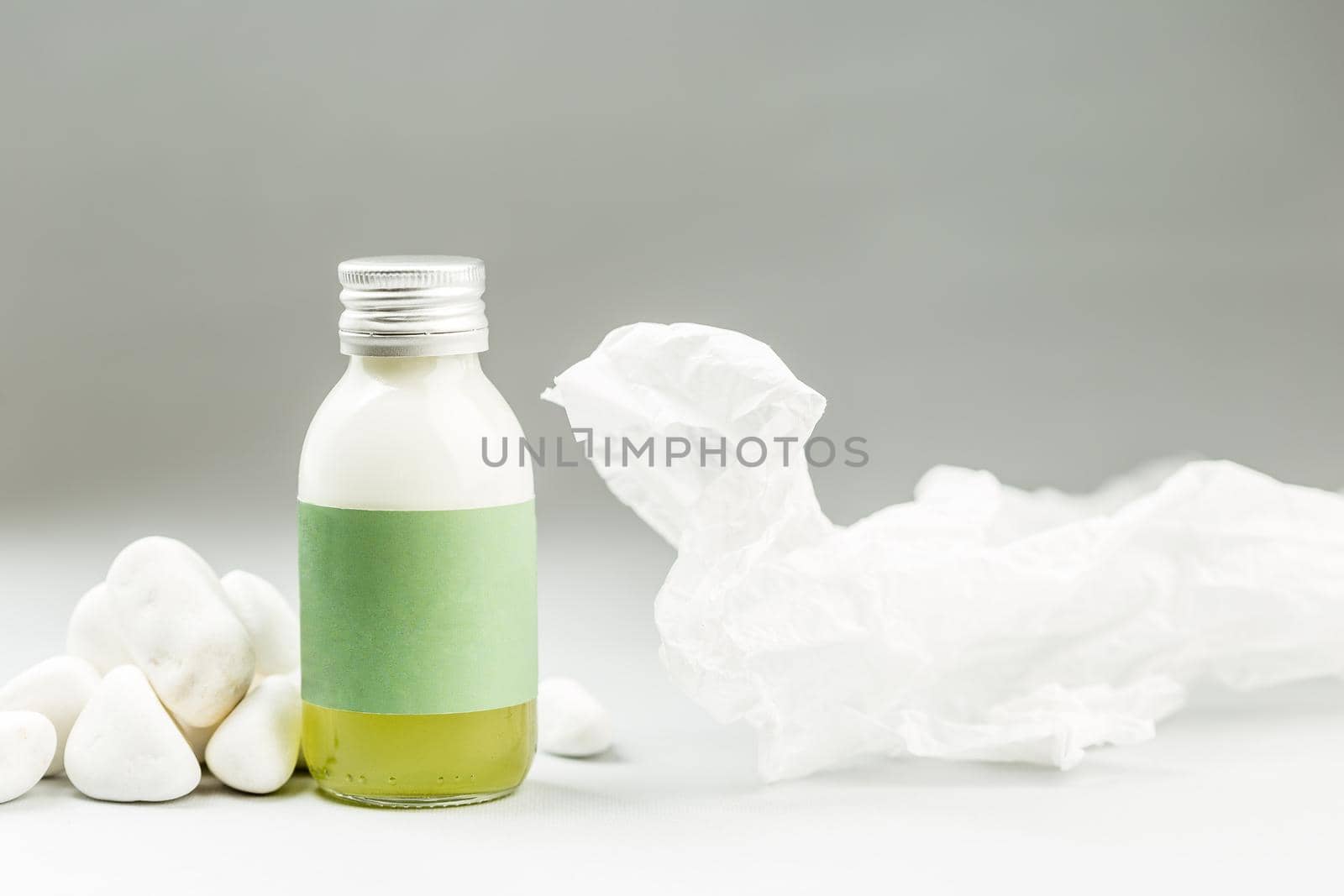 Skin Care Product in Plastic Free Packaging. Glass Bottle with Metal Cap and blank green Label on gray background with white stones and rice paper decoration