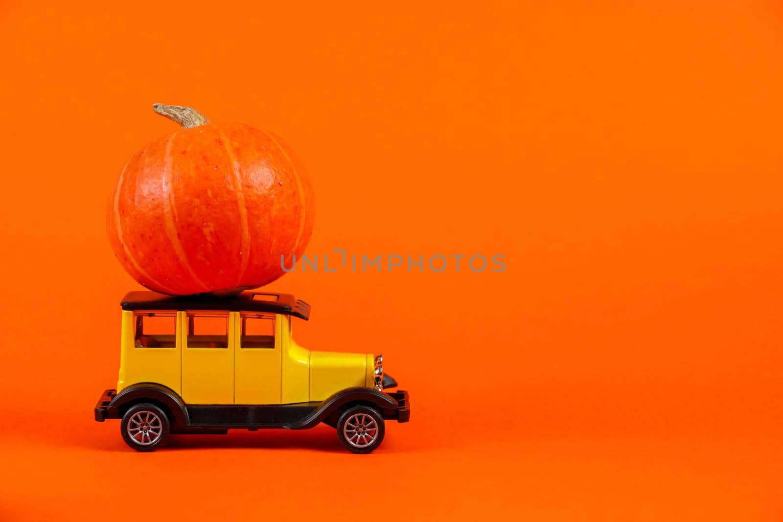Retro toy car with a pumpkin on an orange background. Halloween and autumn harvest concept, place for text.