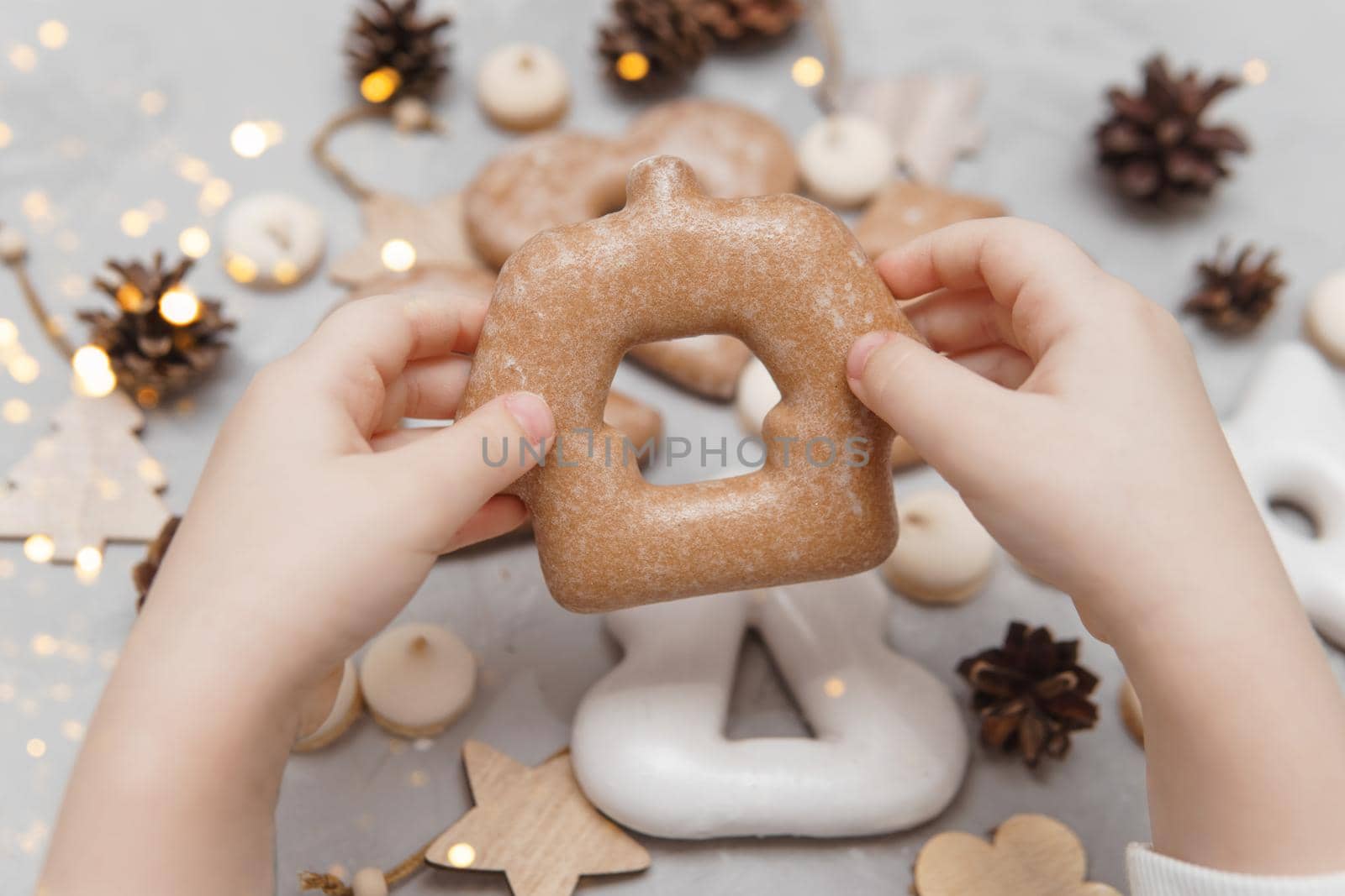 Children's hands hold a gingerbread in the shape of a home. The concept of Christmas sweets, toys, garlands and bokeh. Decor for New Year holidays.