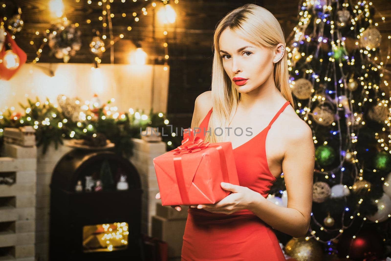 Christmas luxury girl celebrating new year. Blonde Santa girl with christmas bauble ball is posing near Christmas decorated tree