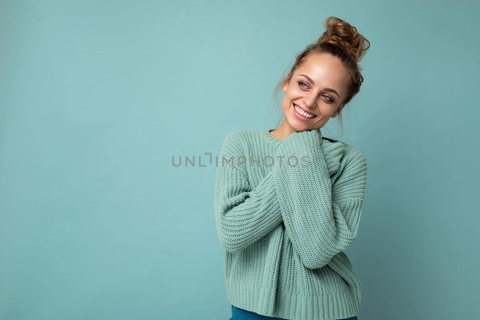 Young beautiful cute curly blonde woman with sexy expression, cheerful and happy face wearing trendy blue sweater isolated over blue background with copy space by TRMK
