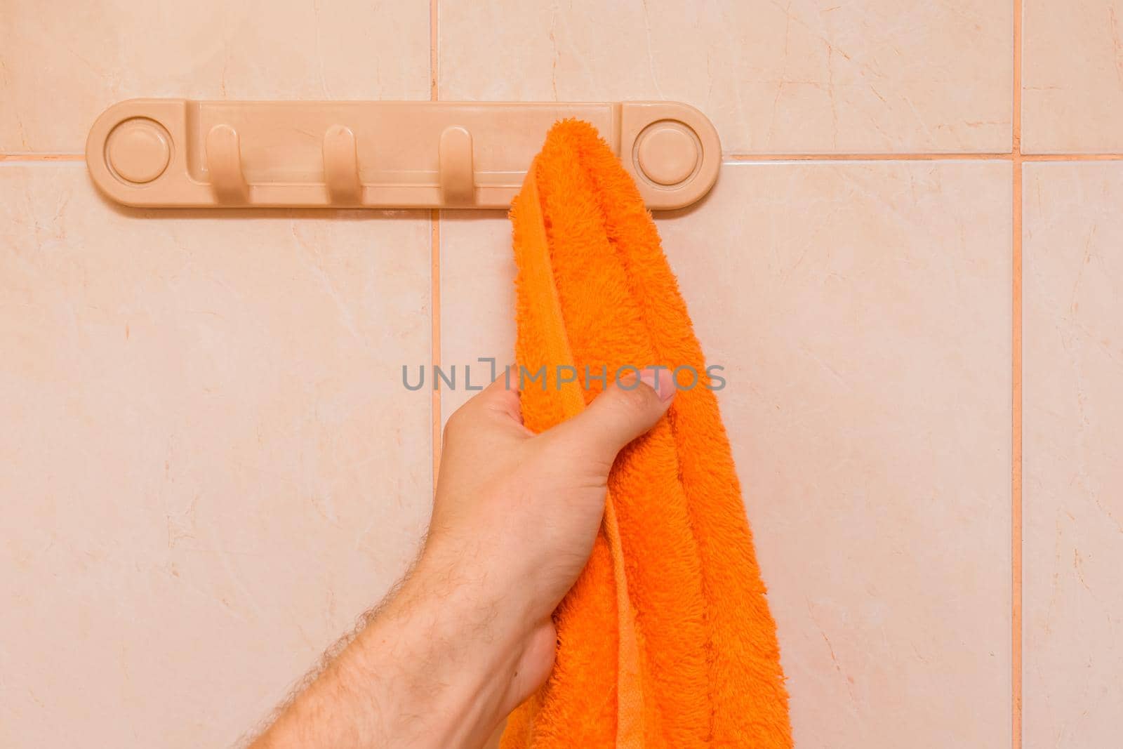 Man's hand takes an orange towel in the bathroom. Care and hygiene concept.