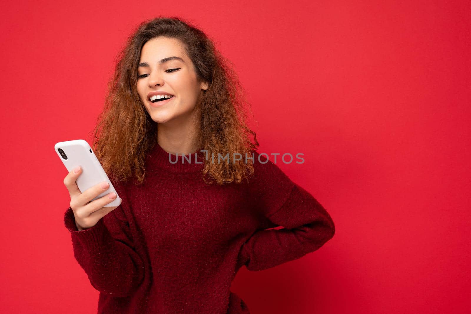 Photo shot of attractive positive good looking young woman wearing casual stylish outfit poising isolated on background with empty space holding in hand and using mobile phone messaging sms looking at smartphone display screen.
