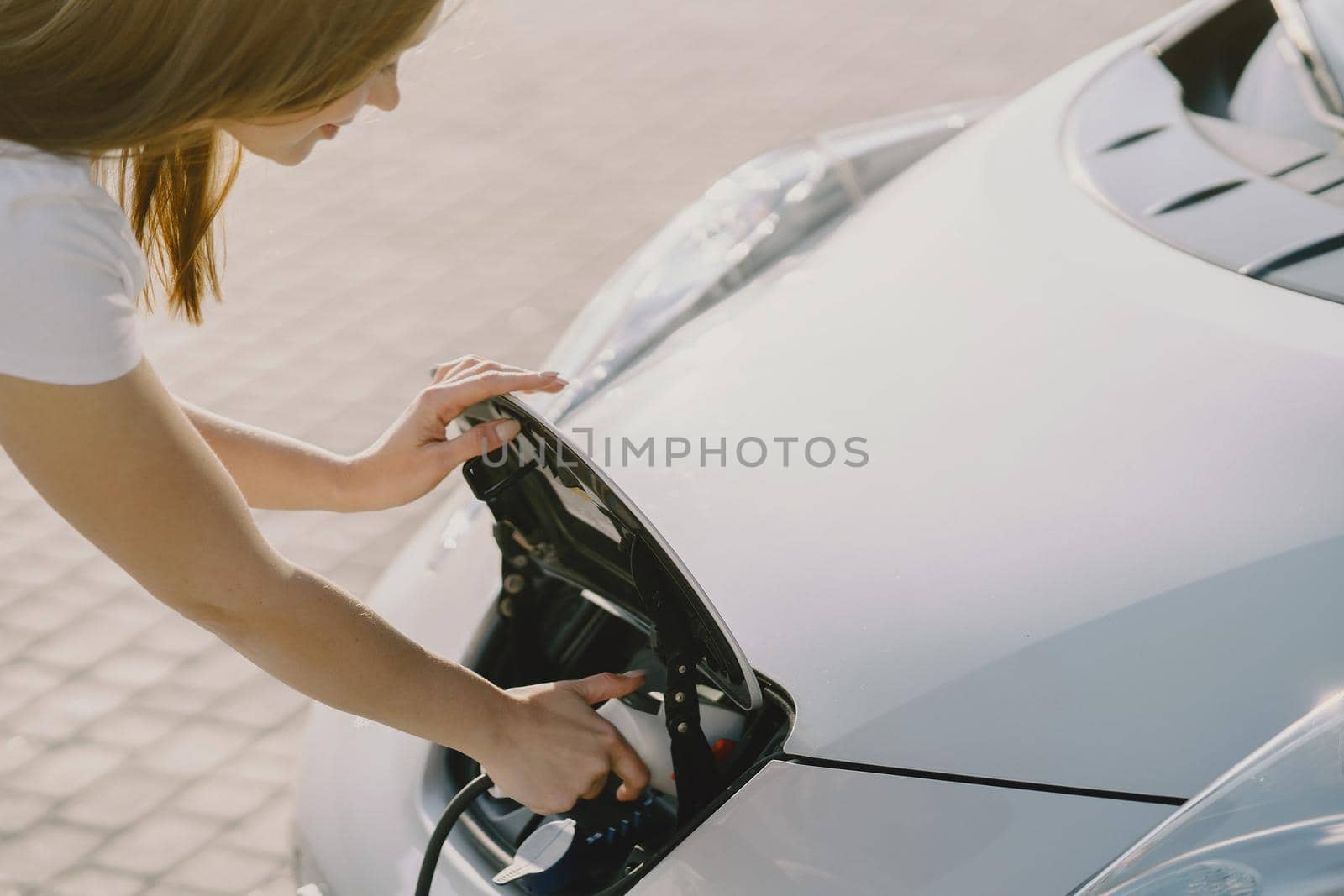 Charging electro car at the electric gas station. Woman standing by the car.