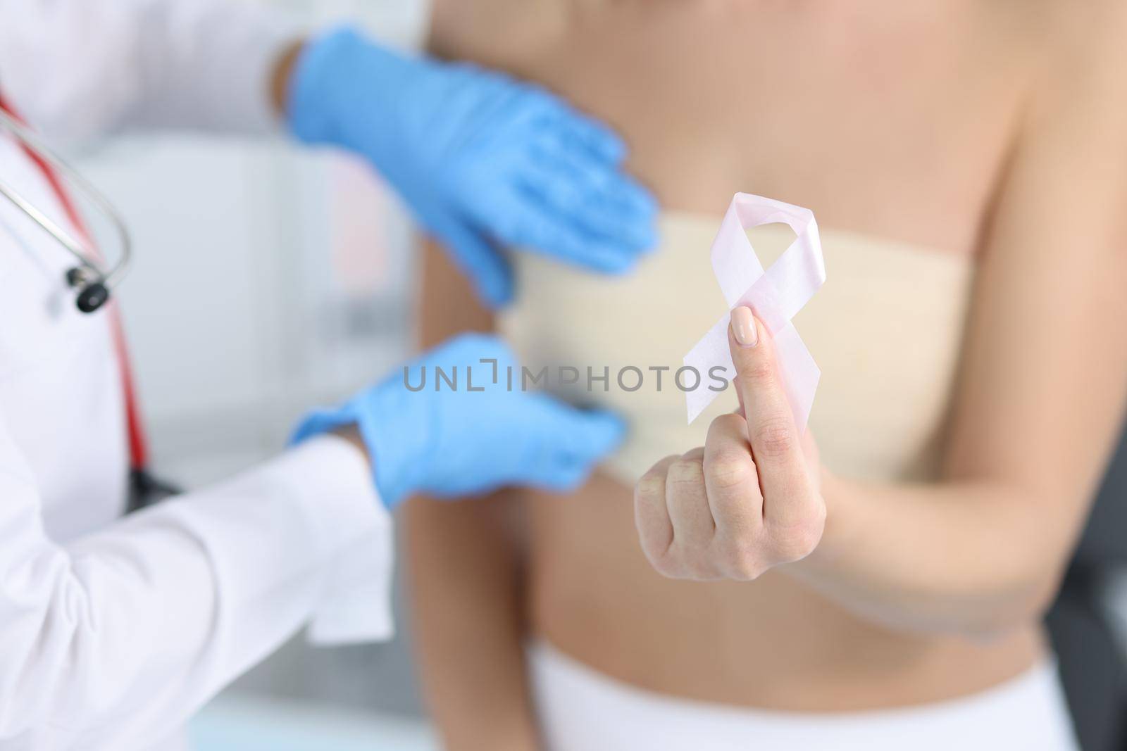Gynecologist conducts medical examination of female breast. Woman holding pink ribbon in hand concept