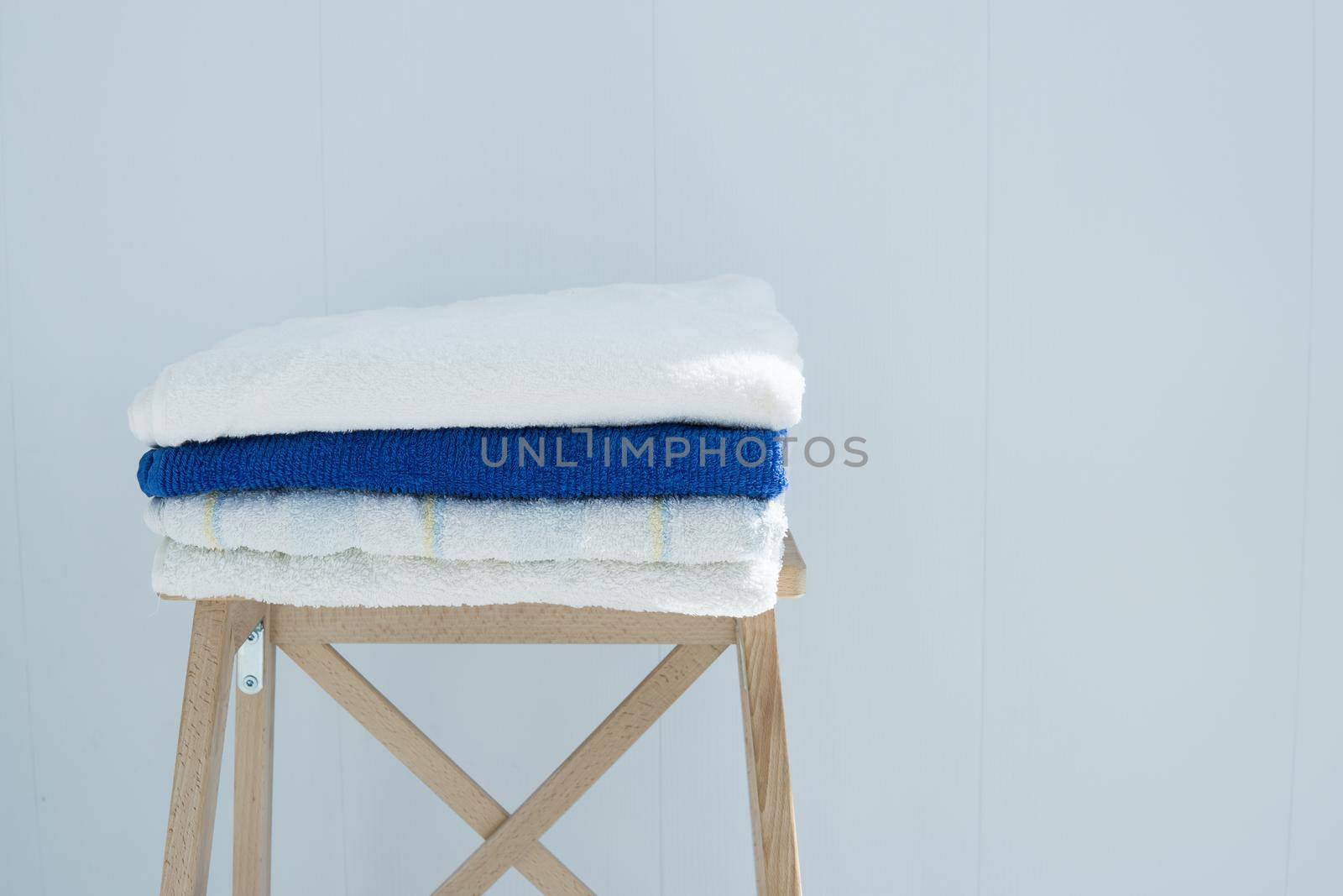 stack of clean bath towels colorful cotton Terry textile stacked on wooden chair near white wall pile concept closeup country style