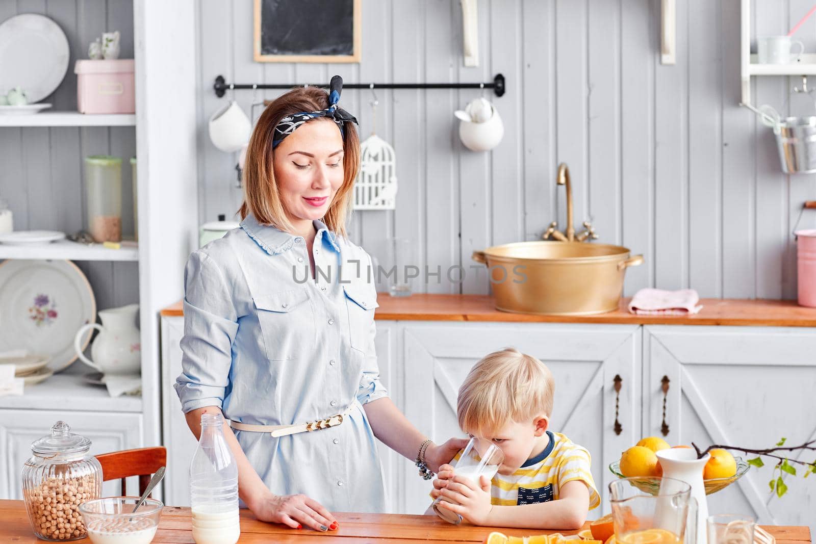 Mother and son are smiling while having a breakfast in kitchen. Mom is pouring milk into glass