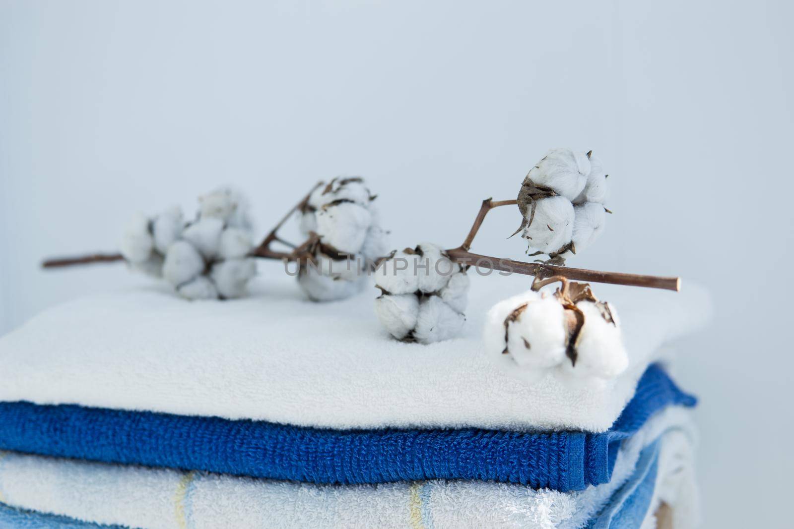 stack of clean bath towels colorful cotton Terry textiles with a sprig of cotton folded on a wooden chair against a white wall nap concept close-up country style