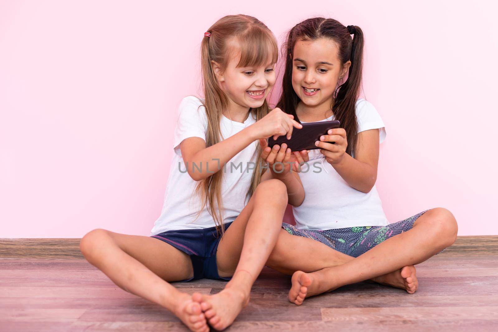Two little girls playing with smartphones on a pink background by Andelov13