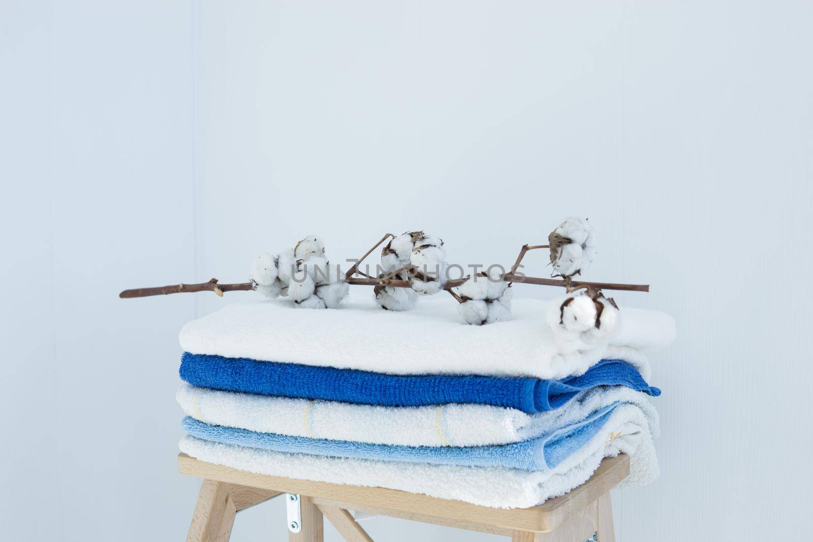 stack of clean bath towels colorful cotton Terry textiles with a sprig of cotton folded on a wooden chair against a white wall nap concept close-up country style.